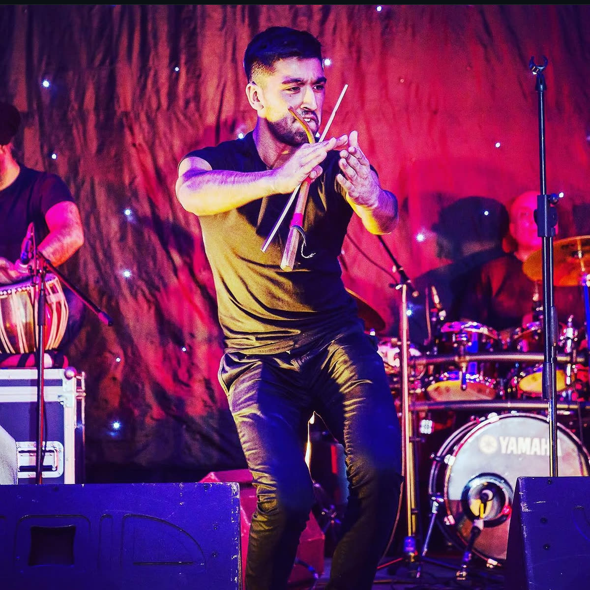 An Achanak musician playing the algoza, the Punjabi double flute, under pink stage lights