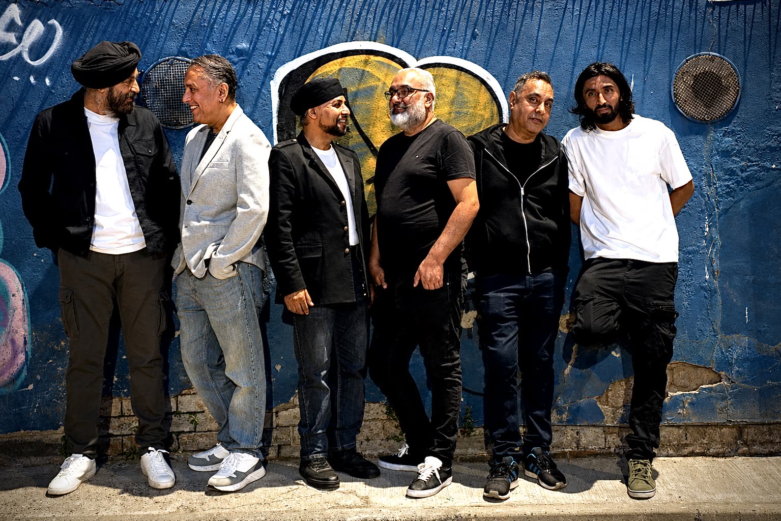 The six members of Achanak standing against a painted blue wall
