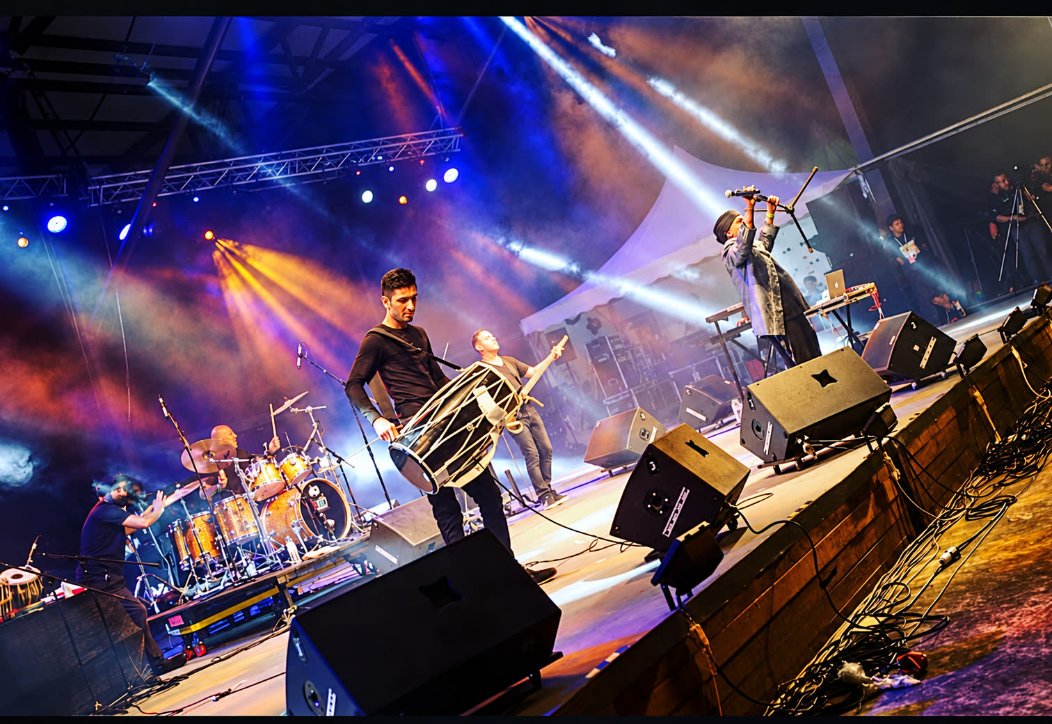 Achanak performing on a festival stage under blue and gold lights, dhol player at the front