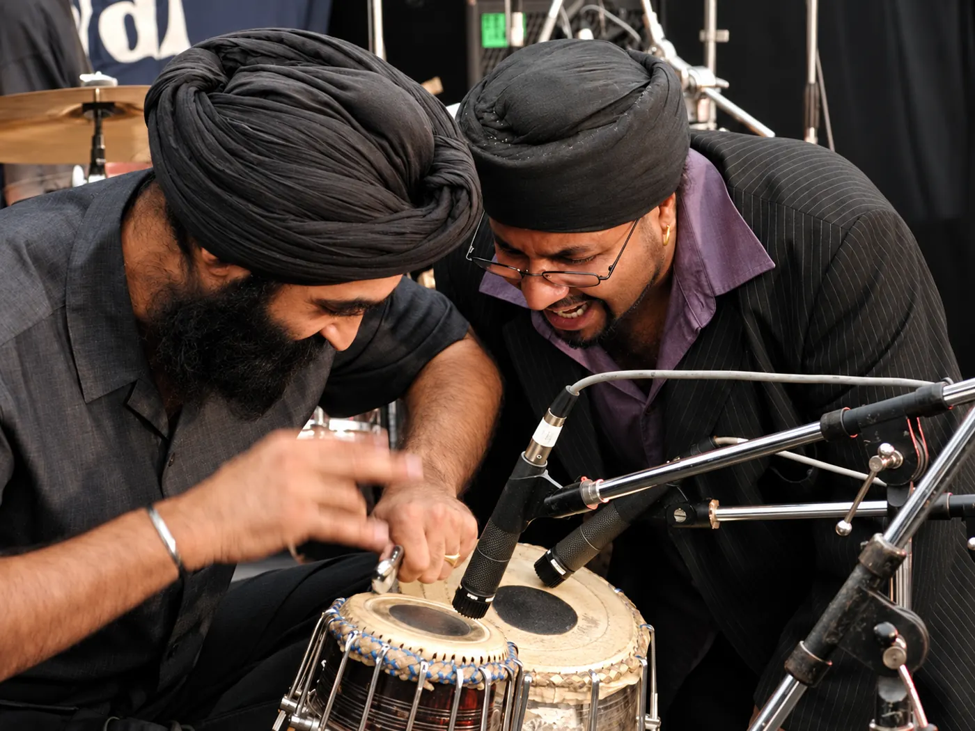 Two turbaned musicians laughing as they play tabla