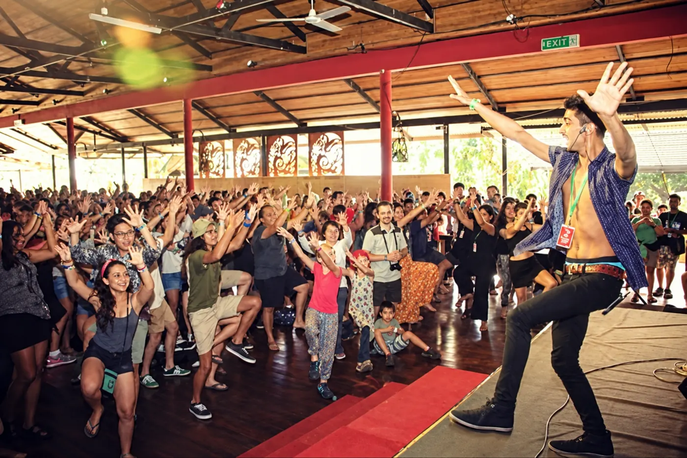 A packed hall of festival-goers with arms raised, dancing with an Achanak dancer on stage