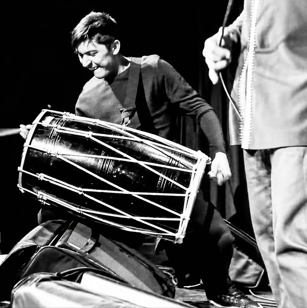 Black and white shot of a dhol player mid-strike